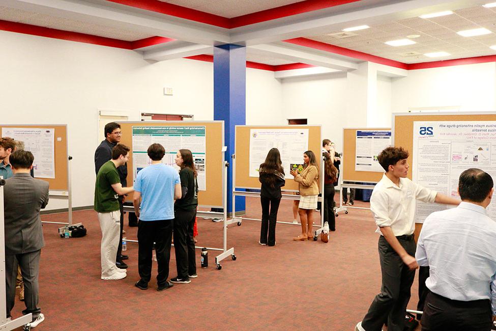 Large room filled with research posters affixed to display boards. People are scattered in groups around the room talking.